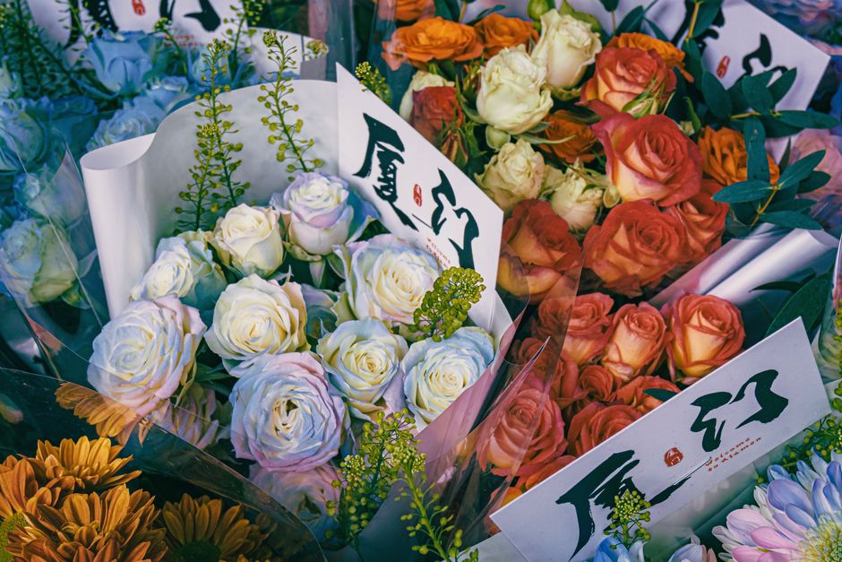 A vibrant arrangement of fresh roses displayed in clear wrapping, featuring creamy white roses with hints of pale pink, complemented by sprigs of green foliage and small yellow-green accents, all arra